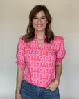 Woman wearing a pink patterned blouse against a plain background