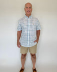 Man wearing a checkered shirt and beige shorts against a white background
