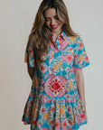 A woman wearing a collared shirtdress with blue, pink and red geometric shapes and colors.