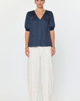 Woman wearing a navy blue blouse and white pants on a white background
