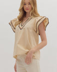 Woman wearing a beige blouse with decorative trim on a white background