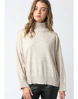 Woman wearing a beige turtleneck sweater against a white background