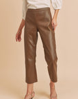 A person wearing high-rise flare vegan leather pants in brown with a white top and heels.