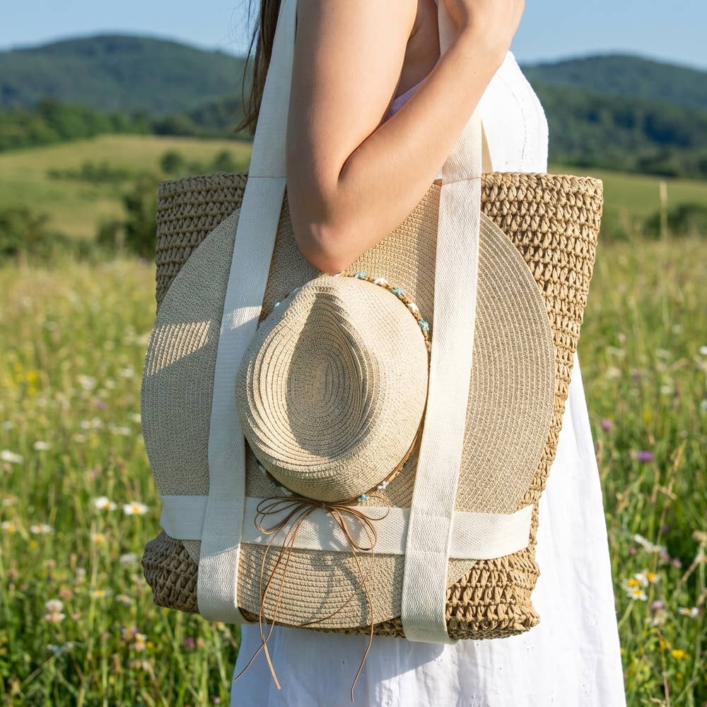 Person holding a straw bag with a hat in a field