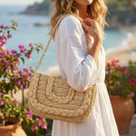 Woman in a white dress holding a woven handbag with a scenic background
