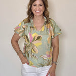 Woman wearing a floral blouse and white pants against a plain background