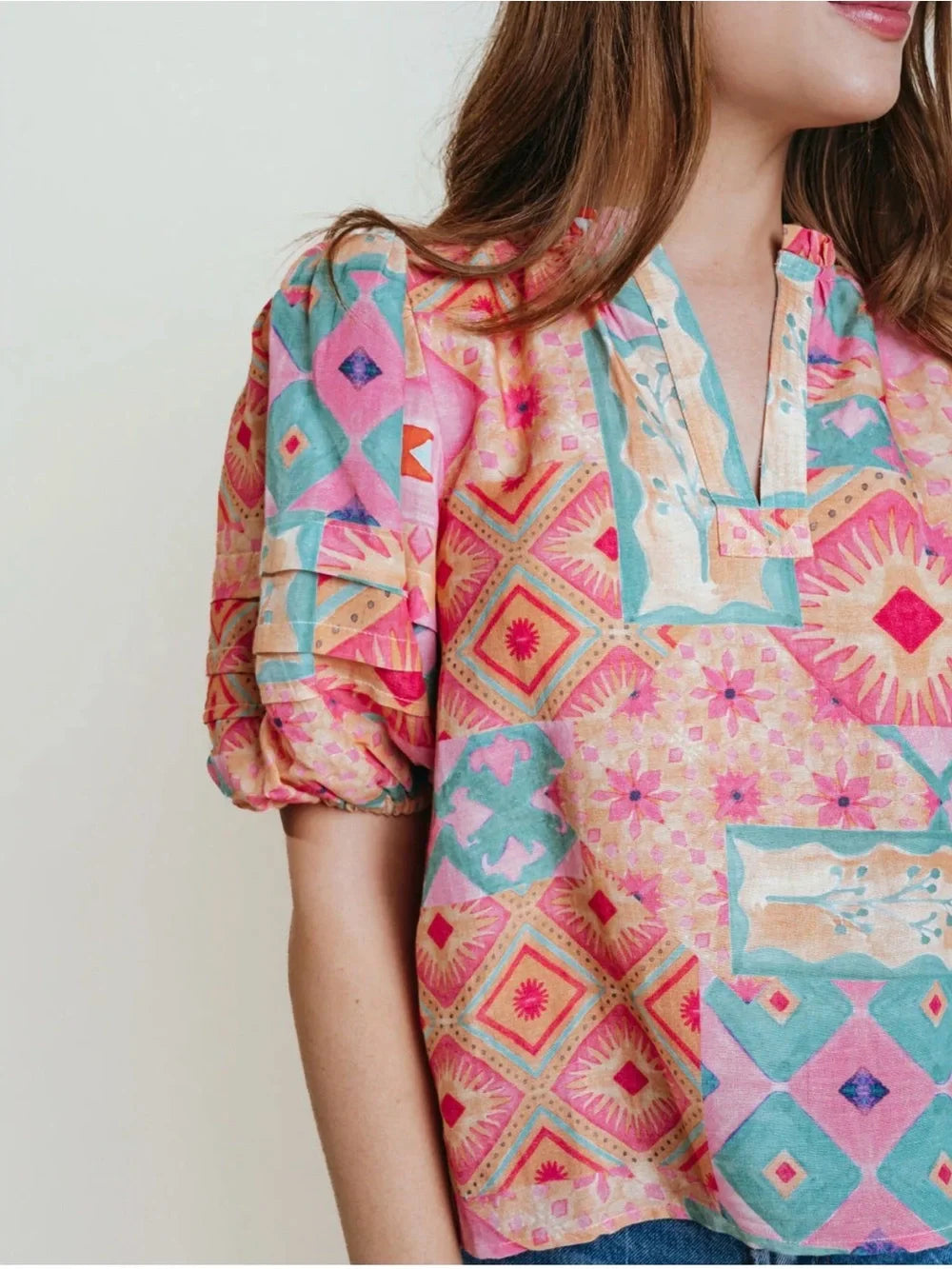 A woman wearing a brightly colored puff sleeve v-neck blouse with oranges, pinks and greens.
