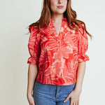 A woman wearing a orange floral v neck blouse with elbow puffy sleeves.