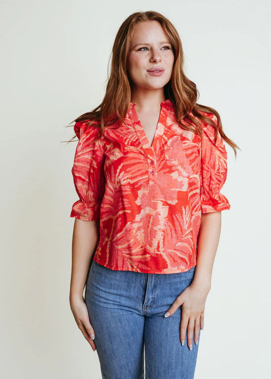 A woman wearing a orange floral v neck blouse with elbow puffy sleeves.
