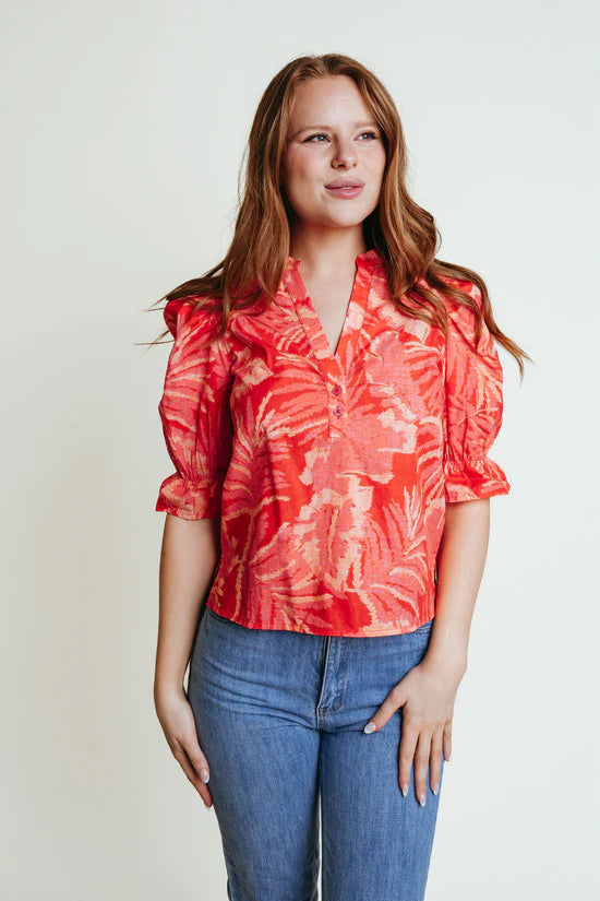 A woman wearing a orange floral v neck blouse with elbow puffy sleeves.