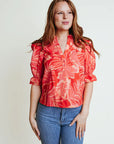A woman wearing a orange floral v neck blouse with elbow puffy sleeves.