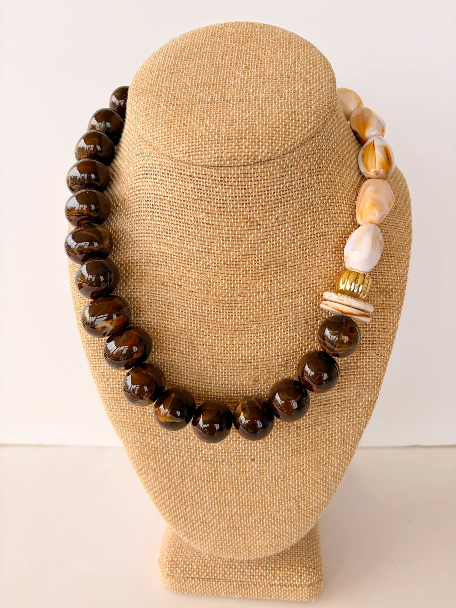 Necklace with brown and beige beads on a tan mannequin bust against a white background