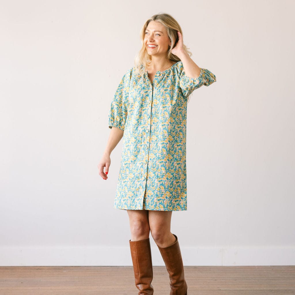 Woman wearing a floral dress and brown boots against a plain background