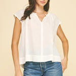 A woman wearing a white v neck blouse with cap sleeves and denim shorts.
