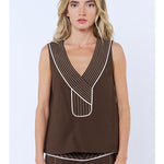 Woman wearing a brown sleeveless top with white trim on a light blue background