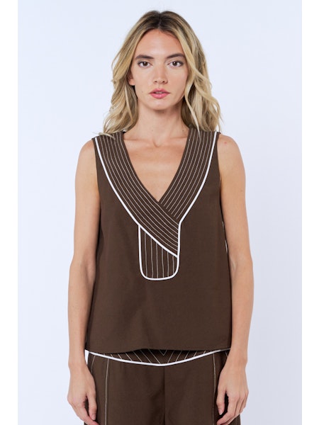 Woman wearing a brown sleeveless top with white trim on a light blue background