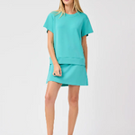 A woman wearing a aqua colored soft material skort with a matching top.