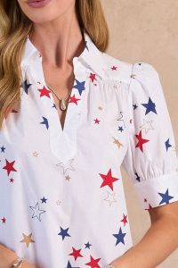 A woman wearing a collared split neck puff sleeve blouse with gold red and navy starts on a white background.