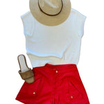 An outfit consisting of red shorts, a white blouse, tan sandals and a tan sun hat.