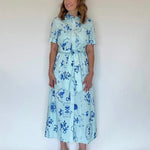 A woman wearing a blue and light blue floral print midi shirtdress with a belt.