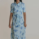 A woman wearing a light blue midi shirtdress with a tie belt.
