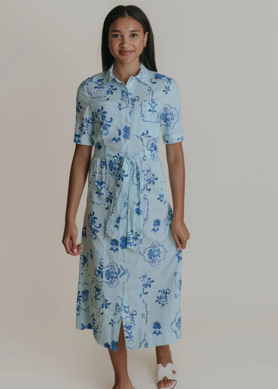 A woman wearing a light blue midi shirtdress with a tie belt.