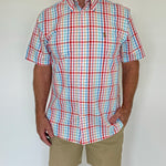 Man wearing a red, blue, and white checkered shirt with beige shorts against a plain background
