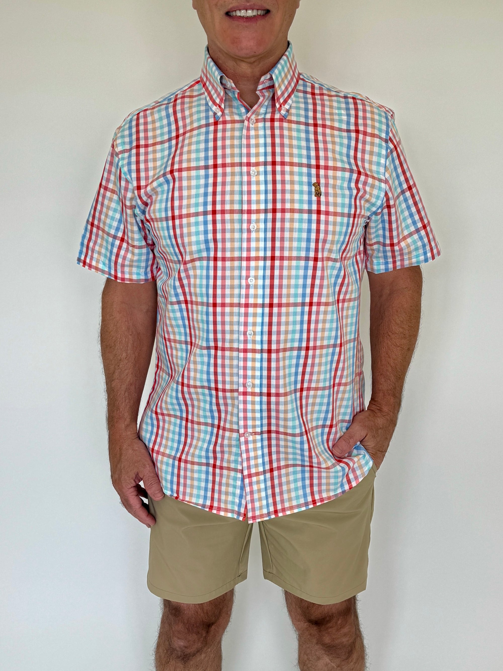 Man wearing a red, blue, and white checkered shirt with beige shorts against a plain background