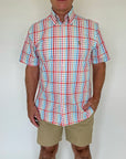 Man wearing a red, blue, and white checkered shirt with beige shorts against a plain background