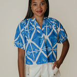 Woman wearing a blue and white patterned shirt with beige shorts on a plain background