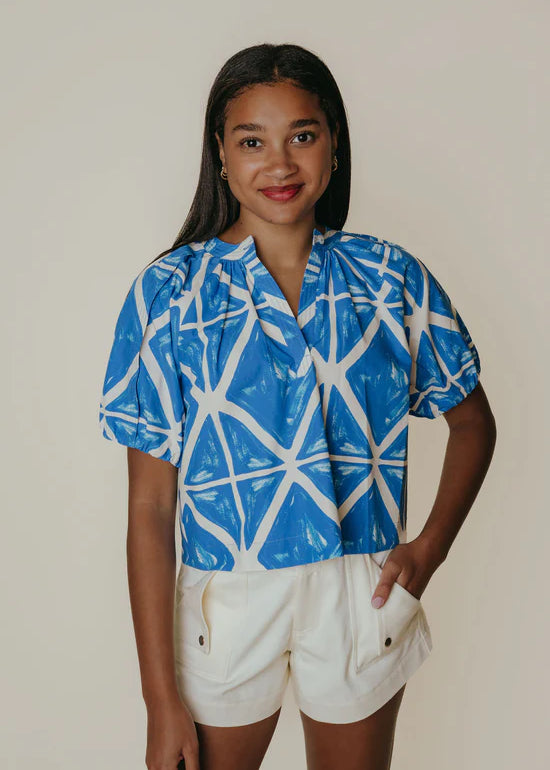Woman wearing a blue and white patterned shirt with beige shorts on a plain background
