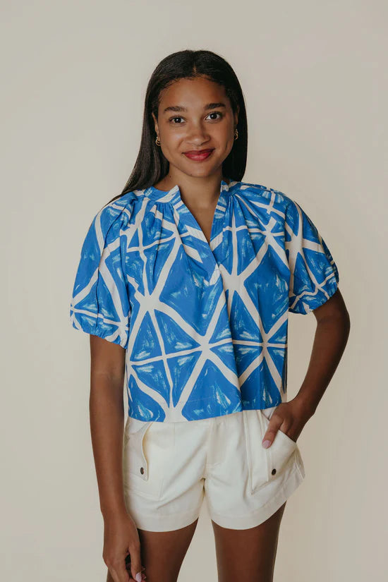 Woman wearing a blue and white patterned shirt with beige shorts on a plain background