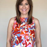 A woman wearing a round neck, sleeveless blouse with a red, blue and pink floral print.