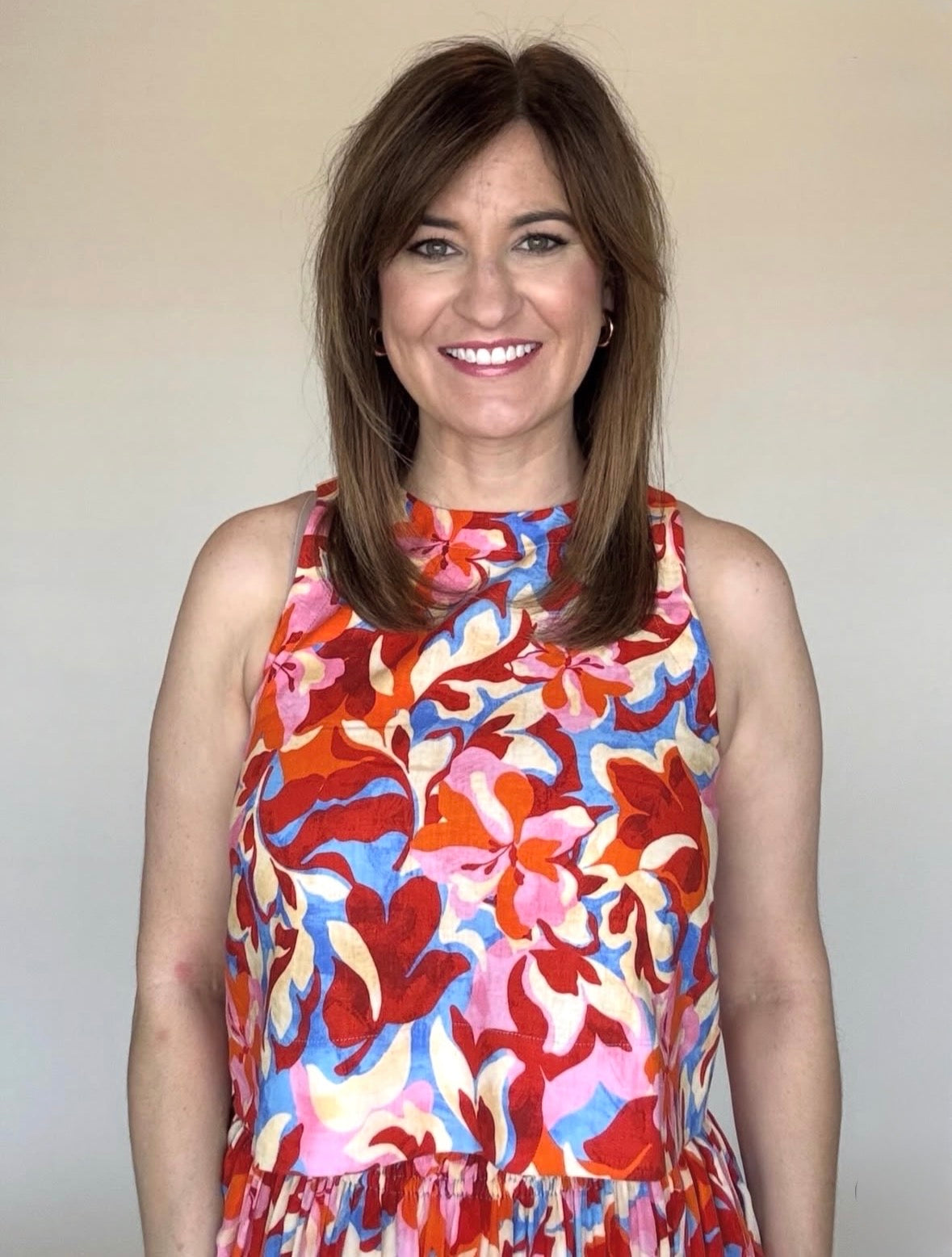 A woman wearing a round neck, sleeveless blouse with a red, blue and pink floral print.