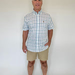 Man wearing a checkered shirt and beige shorts against a white background