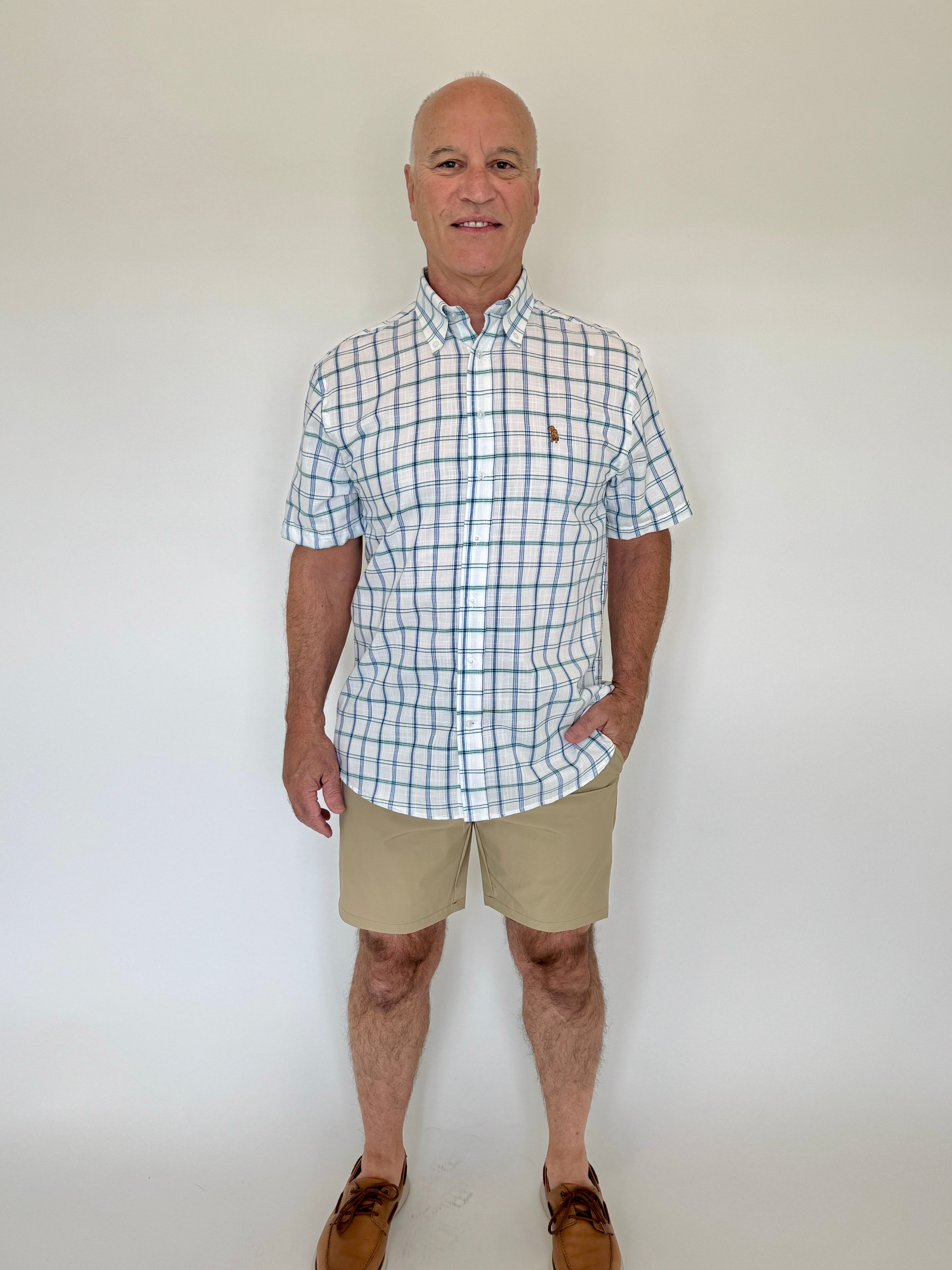 Man wearing a checkered shirt and beige shorts against a white background