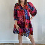 A woman standing and posing in a colorful floral dress with puff sleeves.