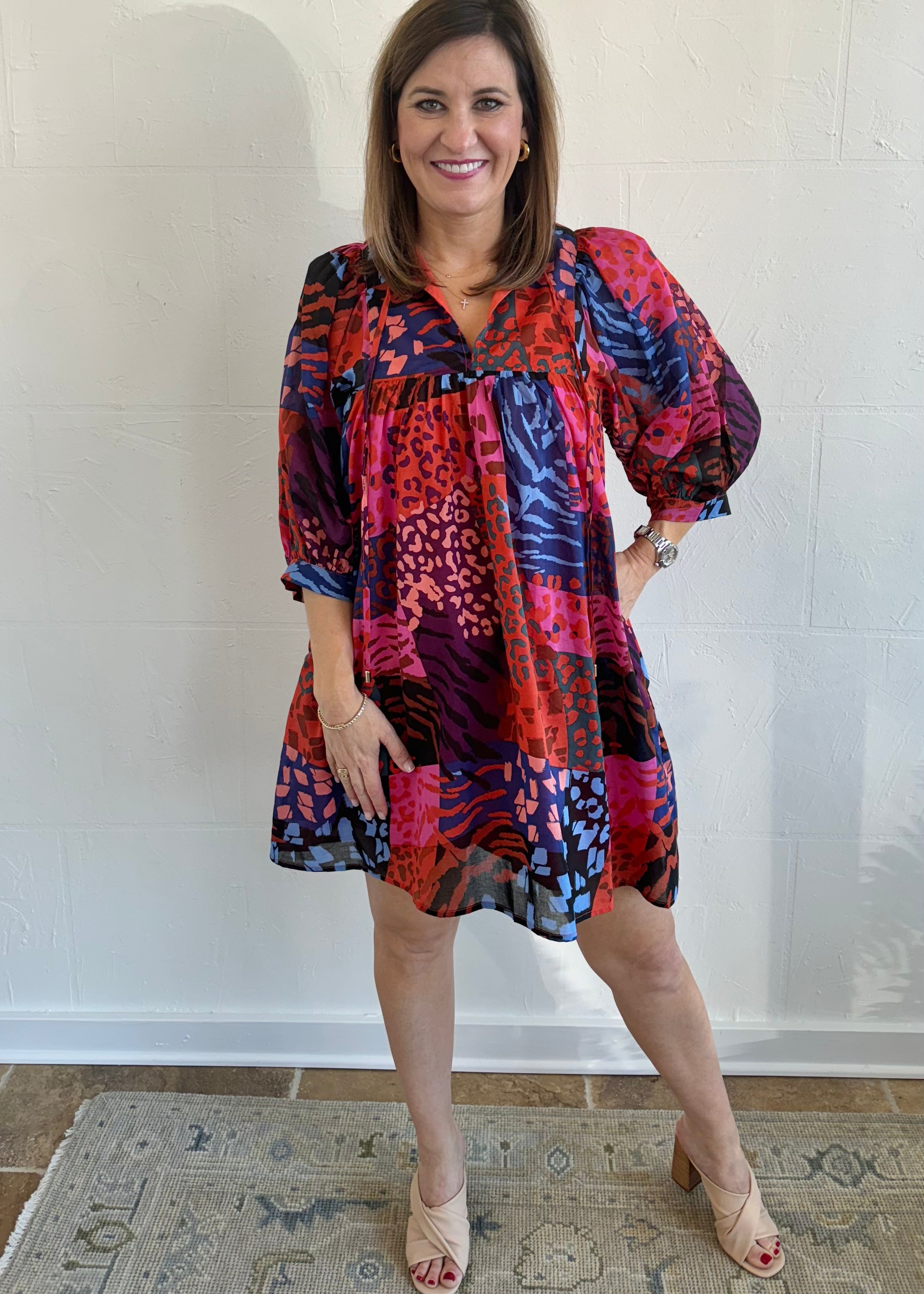 A woman standing and posing in a colorful floral dress with puff sleeves.