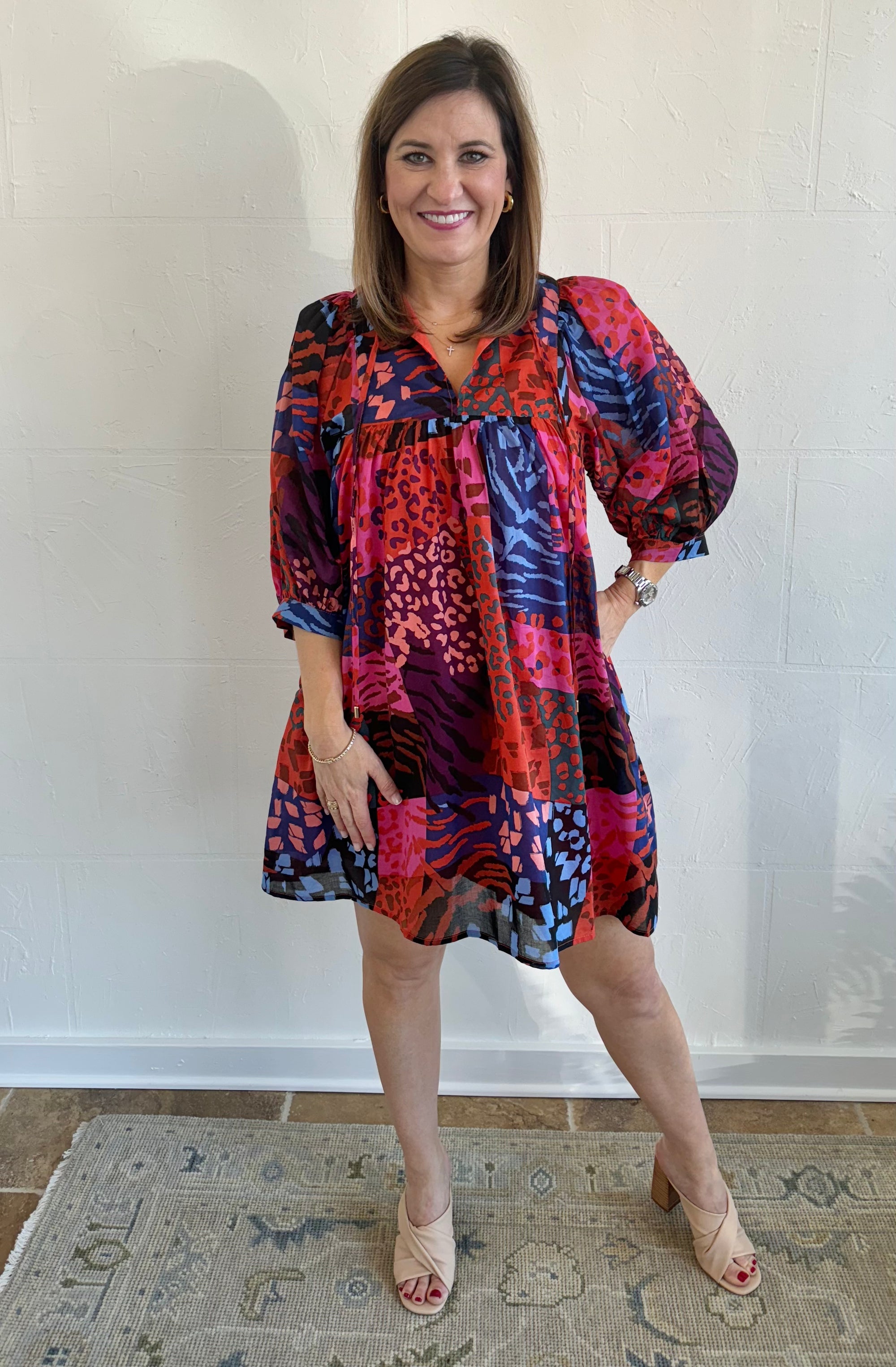 A woman standing and posing in a colorful floral dress with puff sleeves.