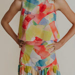 A woman wearing a round neck sleeveless blouse that is mostly yellow with other watercolors.
