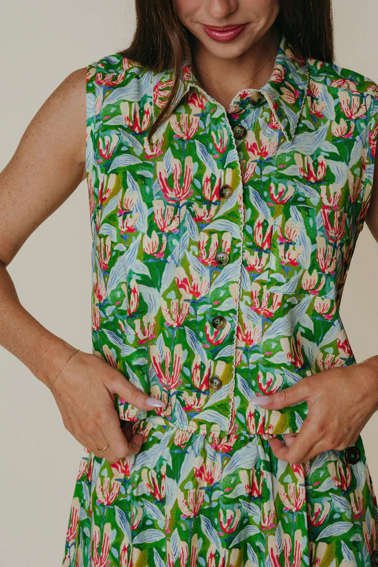 Person wearing a sleeveless dress with a floral pattern on a plain background