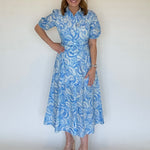 A woman wearing and blue and white seashell print mid dress that has a collar, short sleeves and a belt.