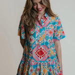 A woman wearing a collared shirtdress with blue, pink and red geometric shapes and colors.