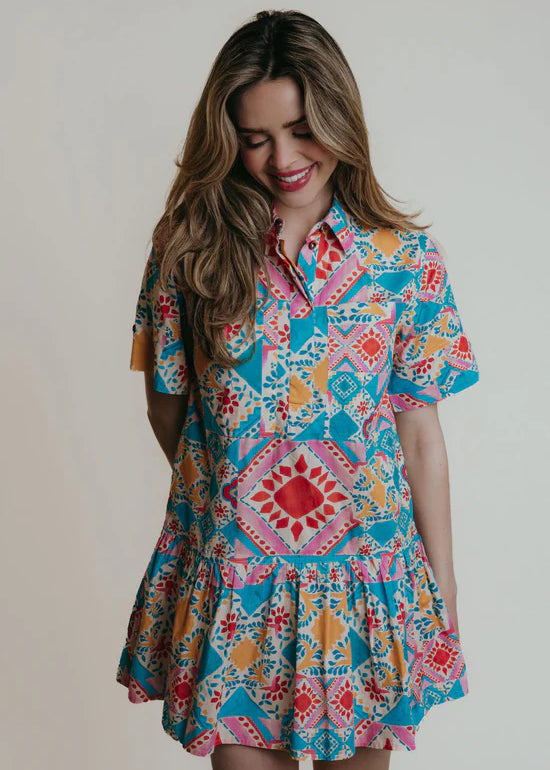 A woman wearing a collared shirtdress with blue, pink and red geometric shapes and colors.