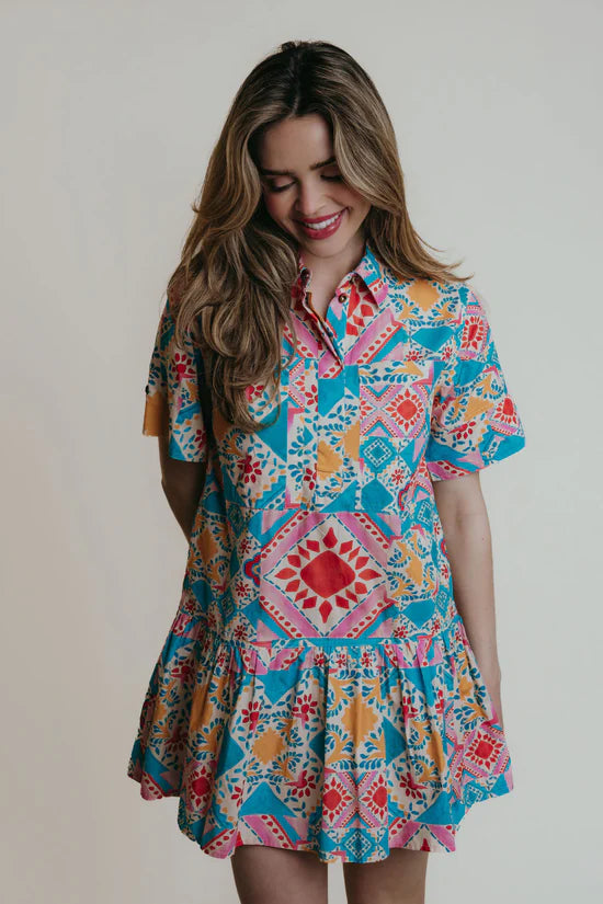 A woman wearing a collared shirtdress with blue, pink and red geometric shapes and colors.