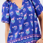 A woman wearing a cobalt blue split neck short sleeve blouse with a floral motif.