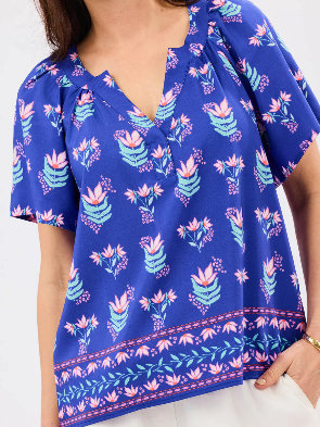 A woman wearing a cobalt blue split neck short sleeve blouse with a floral motif.