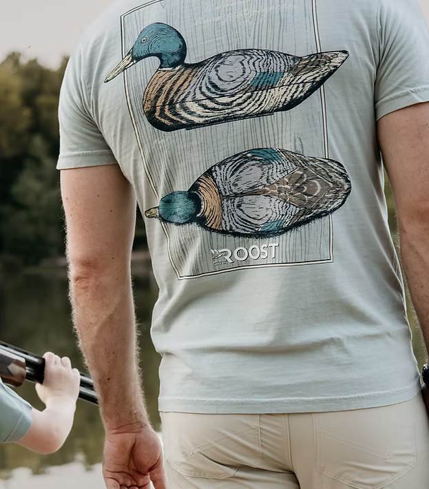 Man wearing a t-shirt with a mallard duck design and 'ROOST' branding outdoors.