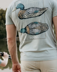 Man wearing a t-shirt with a mallard duck design and 'ROOST' branding outdoors.