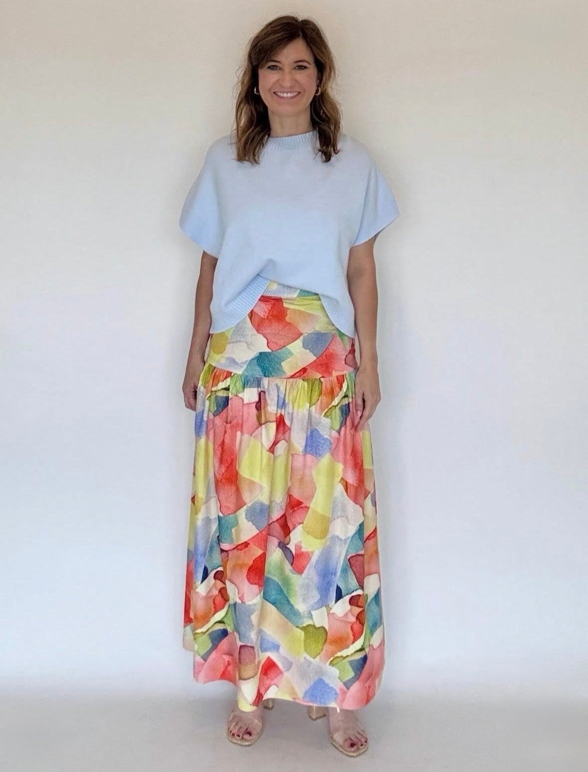 A woman wearing a yellow watercolor print skirt and a blue sweater blouse.